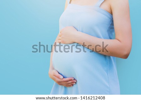 A pregnant woman in a blue dress on a blue background. Pregnancy, parenthood, motherhood concept. Love for children concept with copy space.