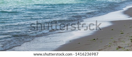 Beautiful summer seascape. Blue sea water surface with green and turquoise tones and shades, foamy waves on the coast, wet beige sand on the beach. Natural colorful pattern, suitable for backgrounds.
