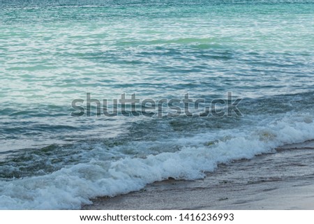 Beautiful summer seascape. Blue sea water surface with green and turquoise tones and shades, foamy waves on the coast, wet beige sand on the beach. Natural colorful pattern, suitable for backgrounds.