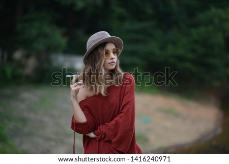 portrait of a smoker girl with sunglasses and hat in the park