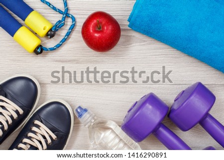 Different tools for fitness with bottle of water and apple in room or gym on gray floor.