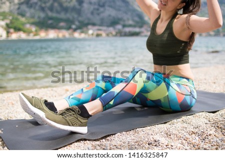 Young beautiful sportive woman sitting on yoga mat, exercising on the beach. Girl meditate by the coast, enjoying the relaxation. Yoga brings her joy