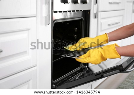 Woman cleaning oven in kitchen Royalty-Free Stock Photo #1416345794