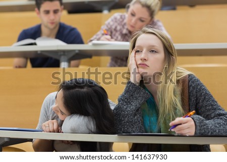 Demotivated students sitting in a lecture hall with one girl napping in college