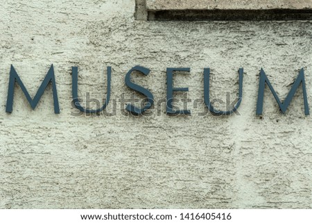 Weathered metal museum sign on plaster wall
