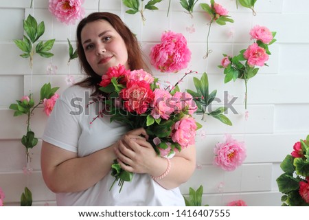 Cute fat girl in jeans and a white T-shirt, posing in the studio with a bright beautiful bouquet of asters. Bright and juicy portrait of a positive girl