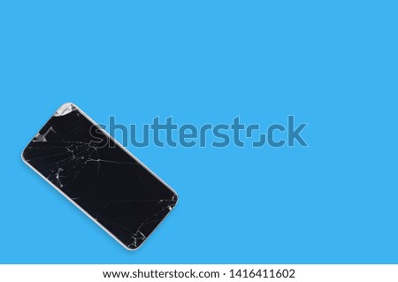 Black crashed smartphone with broken screen and body on blue table in service. Top view. Repair concept. Copy space