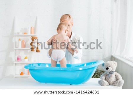 blonde mother holding in arms toddler kid in bathroom 