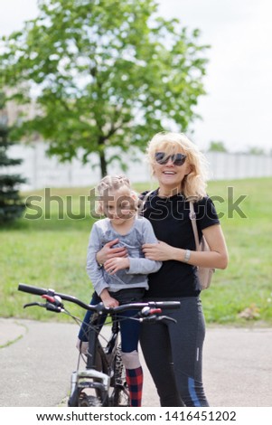 Happy family in the summer park. Mother teaches her daughter to ride a bicycle in the park.Looking at camera