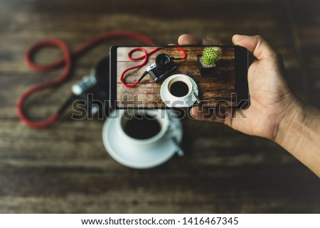 Hand holding smart phone taking photo of coffee and camera on wooden table.