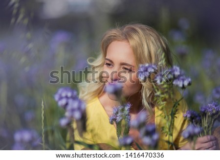 Young beautiful woman blonde in a hat walks through a field of purple flowers. Summer. Spring.