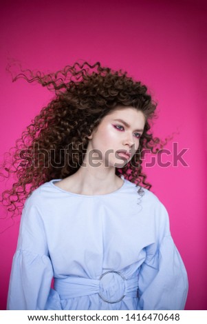 Curly hair girl in blue blouse on pink background. Fashion model with curly hair. Beautiful young girl with curly hair. Curly hair girl on pink background.