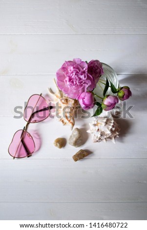 Pink glasses, peonies and sea shells on a white wooden table. Romantic summer flat lay.