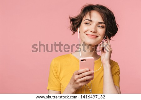 Image of a happy young beautiful woman posing isolated over pink wall background listening music with earphones using mobile phone. Royalty-Free Stock Photo #1416497132
