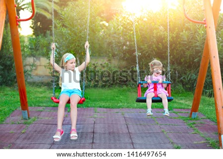 Children playing on playground in park. Two little sisters on the swing