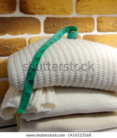 Stack of folded white sweaters, measuring tape