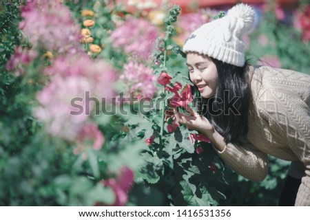 Beautiful happy young asian woman wearing warm clothing amidst flower garden during sunny day.