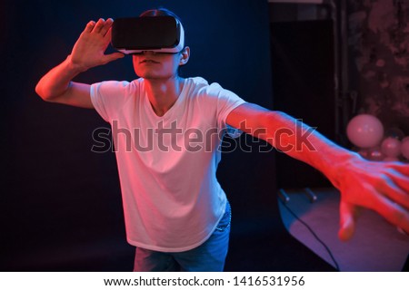 This is unbelievable. Young man using virtual reality glasses in the dark room with neon lighting.