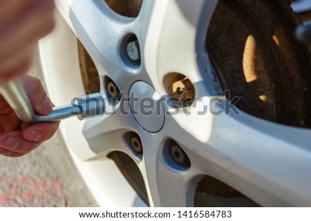 Close-up hands with cylinder wrench unscrew damaged wheel of car. Man changes flat wheel after car breaks down. Wheel balancing, repair and replacement car tires on wheels. Tire installation concept