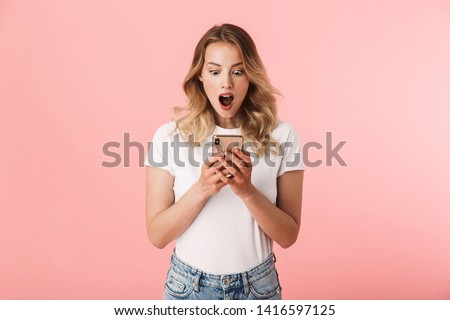 Image of a beautiful shocked young blonde woman posing isolated over pink wall background using mobile phone.