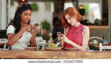 Diverse young women taking photo of food plate looking at smartphone device
