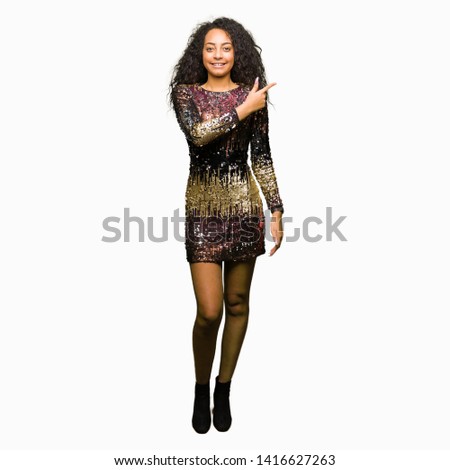 Young beautiful girl with curly hair wearing night party dress cheerful with a smile of face pointing with hand and finger up to the side with happy and natural expression on face