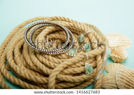 Beautiful composition consists of silver jewellery bracelets broach like lizard necklace ring earring set with green stoun all lies on nest from rope and cyan surface with shells