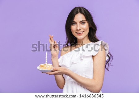 Beautiful cheerful young woman wearing summer outfit standing isolated over violet background, celebrating birthday with cake