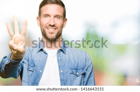 Handsome man with blue eyes and beard wearing denim jacket showing and pointing up with fingers number three while smiling confident and happy.