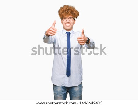 Young handsome business man with afro wearing glasses approving doing positive gesture with hand, thumbs up smiling and happy for success. Looking at the camera, winner gesture.
