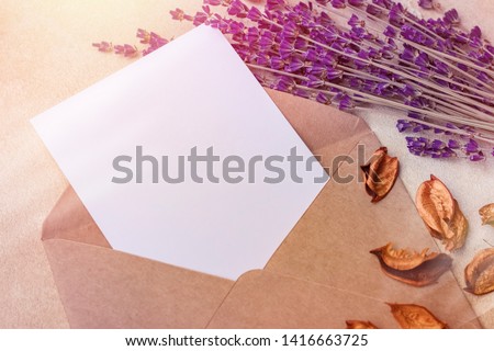 Blank sheet of paper in Kraft envelope and lavender flowers on a light background. Simple wedding arrangement. mock up