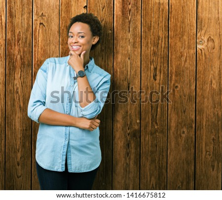 Young beautiful african american woman over isolated background looking confident at the camera with smile with crossed arms and hand raised on chin. Thinking positive.
