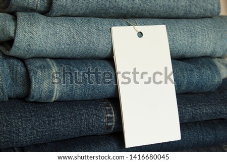 A stack of new jeans with white paper tag mockup and copy space