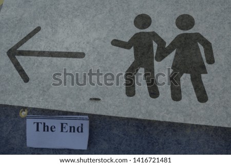 Sign for pedestrian safety, a man and a woman figure holding hands and an arrow above the words 'the end'