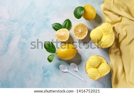 two portions lemon ice cream in paper cup and fresh lemon on mint colors background ,top view