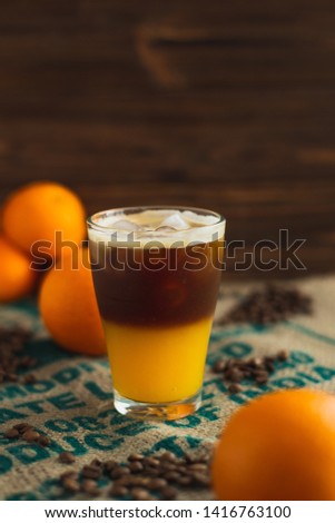 cold brew coffee with orange juice. Glass with cold coffee and ice on the background of a bag  and chaotically scattered coffee beans and orange. Selective focus