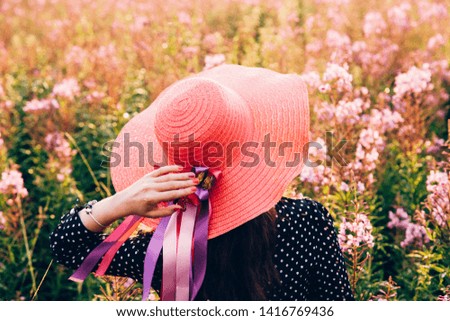 Young woman walking  in the summer flower field wearing straw hat. Bright sunlight beautiful nature