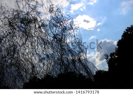 Metal wire mesh wavy close up abstract art with blue cloudy sky background.