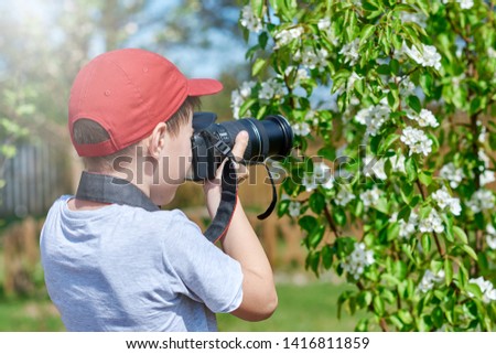 Schoolboy is taking picture of blossoming trees in the countryside garden.