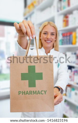 Pharmacist holding paper bag with a green Pharmacy logo in a drugstore Royalty-Free Stock Photo #1416823196