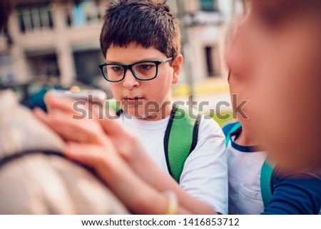 Boy wearing eyeglasses taking close-up photos of small bug on a jacket if his friend with a smart phone