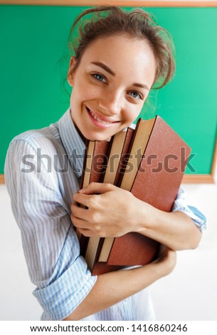 Smiling student hugging books. Photo of teen girl near blackboard, education concept