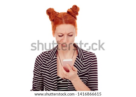 Skeptical woman looking at mobile phone texting receiving surprising message looking at photos in social media, isolated on white background, wearing striped black white jacket with 2 buns up hairdo