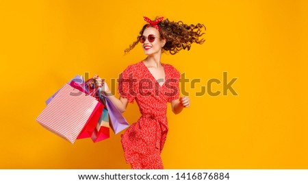 concept of shopping purchases and sales of happy young girl with packages in red dress on yellow background
