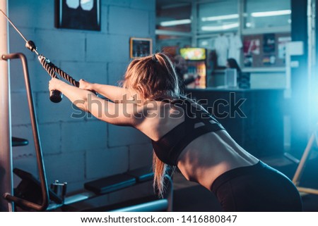 Concept of healthy lifestyle and workouts. young athletic girl is engaged on the simulator for training the muscles of the back. from the side view