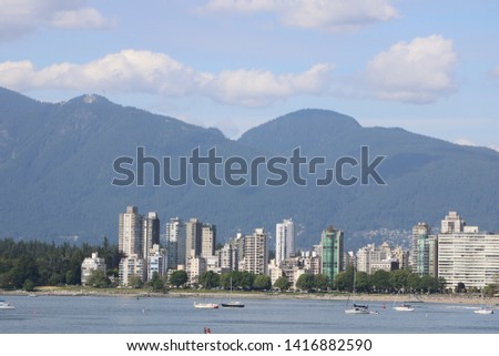 Skyline of Vancouver's Westend with beaches and ocean in the foreground with mountains and a summer sky in the background.