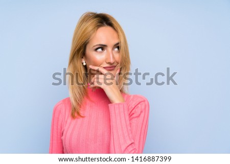 Young blonde woman with pink sweater over isolated blue background thinking an idea