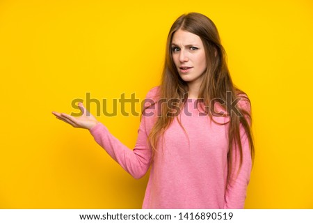 Young woman with long hair over isolated yellow wall making doubts gesture