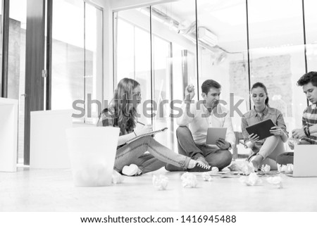 Black and White photo of Businessman throwing paper balls while discussing with colleagues in office