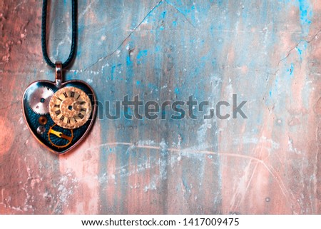 on the old ancient wall there is a pendant in the shape of a heart on a rope, and inside it is an old clock mechanism; concept photo show that eternal love is timeless
